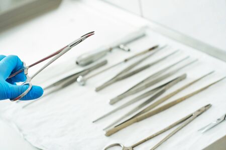 Hand of a nurse in a blue medical glove is holding the clip. Medical instruments for surgery are on...