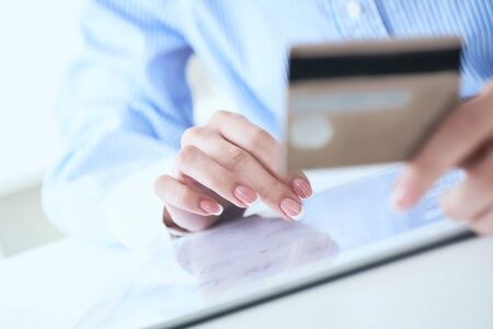 Close-up womans hands holding a credit card and using tablet pc for online shopping. Middle section of young businesswoman making online payments with credit card and tablet.の写真素材