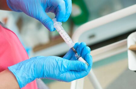 Close-up hands of young woman doctor anesthesiologist dressed in pink gown, blue gloves prepares...