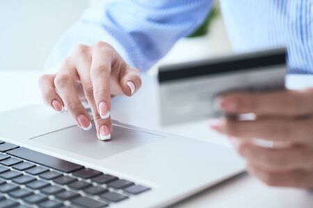 Female hands holding credit card and typing numbers on laptop keyboard while sitting at office...