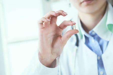 Young female doctor or nurse holding a yellow transparent pill in hand. Doctor presents a new medicine to a patient.の写真素材