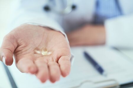 Young female doctor or nurse holding a yellow transparent pill in hand. Doctor presents a new medicine to a patient.の写真素材
