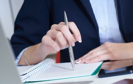 Young businesswoman holding pen in hand while reading information at laptop screen. Female hands holding a pen and making notes close up.の写真素材