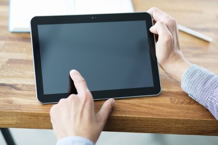 Mans hands holding blank tablet device over a wooden workspace table.の写真素材