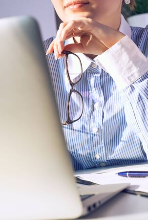 Thoughtful female office manager with spectacles in hand near the chin looking at laptop screen sitting at working place. Contemplative businesswoman thinking about idea for startup project.の写真素材