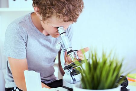 Cute elementary schoolboy looking into microscope at his desk in the laboratory. Young scientist making experiments in laboratory. Child and science. Education concept.の写真素材