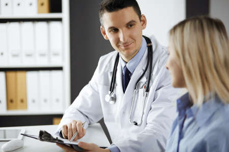 Friendly male doctor and patient woman discussing current health examination while sitting in...