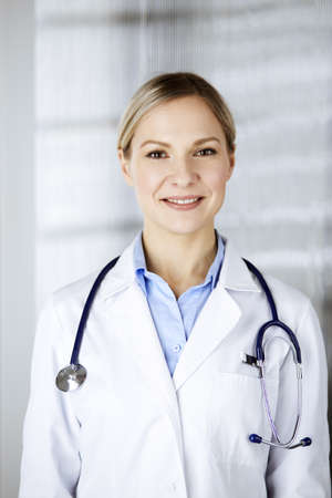 Friendly female doctor standing in clinic. Portrait of cheerful smiling physician. Perfect medical service in hospital. Medicine and healthcare conceptの写真素材