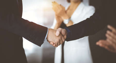 Unknown businesspeople are shaking their hands after signing a contract, while standing together in...