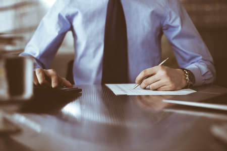 Unknown man accountant in blue shirt use calculator and computer with holding pen on while staying...
