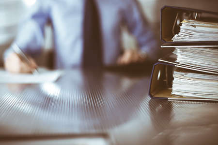 Binders with papers are waiting to be processed by man accountant in blue shirt staying at home during covid pandemic. Taxes and audit conceptの写真素材