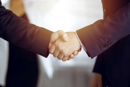 Unknown businesspeople are shaking their hands after signing a contract, while standing together in...