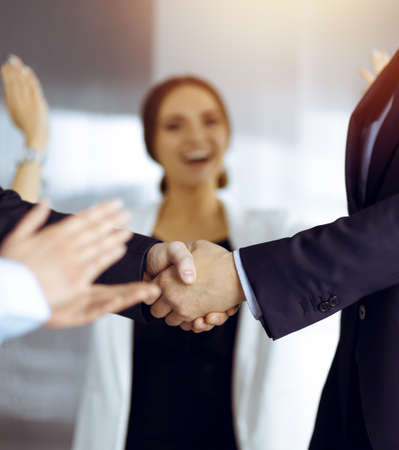 Unknown businesspeople are shaking their hands after signing a contract, while standing together in a sunny modern office, close-up. Business communication conceptの写真素材