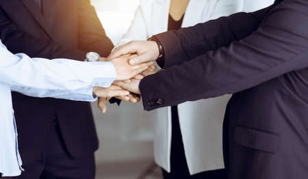 Group of unknown businesspeople are joining hands in a sunny modern office. Unknown businessmen are making circle with their hands. Concept of trust and support in a businessの写真素材