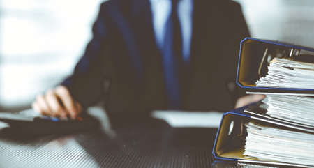 Binders with papers are waiting to be processed by man accountant in blue blazer staying at home during pandemic. Taxes and audit concept. Internal Revenue Service inspector checking financial document.の写真素材