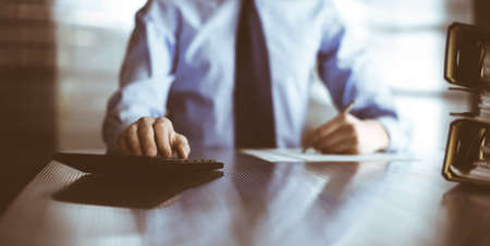 Unknown man accountant in blue shirt use calculator and computer with holding pen on while staying...
