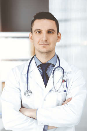 Male doctor standing straight with arms crossed in clinic near his working place. Perfect medical service in hospital. Medicine and healthcare conceptの写真素材