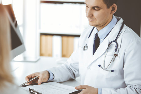 Friendly male doctor and patient woman discussing current health examination while sitting in clinic. Perfect medical service in hospital. Medicine and healthcare conceptの写真素材