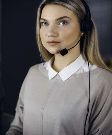 Diverse people group in call center. Blonde business woman talking by headset while sitting in modern office. Telemarketing and customer service conceptの写真素材