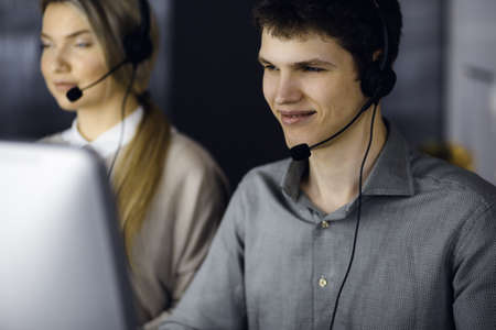 Diverse people group in call center. Businessman talking by headset while sitting in modern officeの写真素材