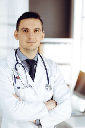 Male doctor standing straight in sunny clinic. Perfect medical service in hospitalの写真素材