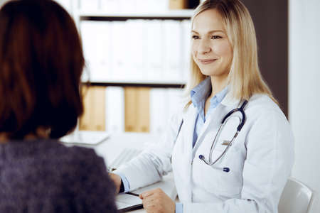 Friendly female doctor and patient woman discussing current health examination while sitting in sunny clinic. Perfect medical service in hospitalの写真素材