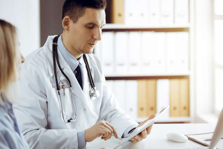 Friendly female doctor and patient woman discussing current health examination while sitting in sunny clinic. Perfect medical service in hospitalの写真素材