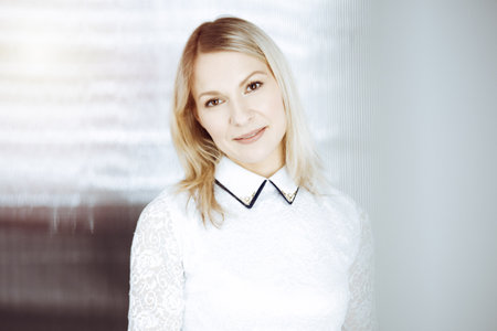 Friendly adult business woman standing straight. Business headshot or portrait in sunny officeの写真素材
