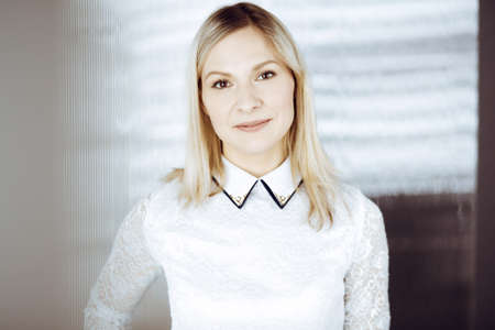 Friendly adult business woman standing straight. Business headshot or portrait in sunny officeの写真素材