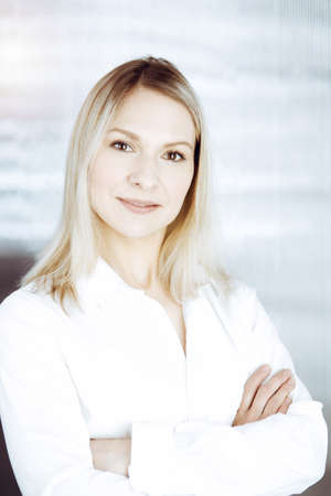 Friendly adult business woman standing straight. Business headshot or portrait in sunny officeの写真素材