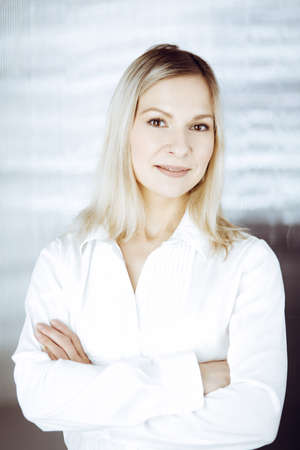 Friendly adult business woman standing straight. Business headshot or portrait in sunny officeの写真素材