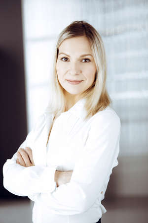 Friendly adult business woman standing straight. Business headshot or portrait in sunny officeの写真素材