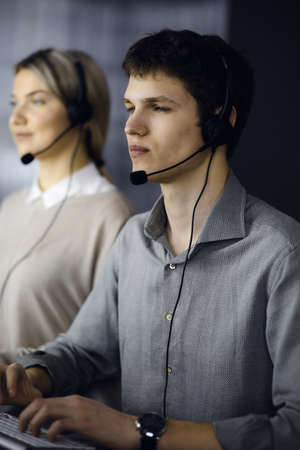 Diverse people group in call center. Businessman talking by headset while sitting in modern officeの写真素材