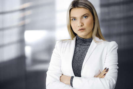 Young blonde business woman or female student in white blazer is standing straight and posing at camera. Lifestyle and diverse people conceptの写真素材