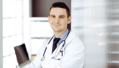 Male doctor standing straight in sunny clinic. Perfect medical service in hospitalの写真素材