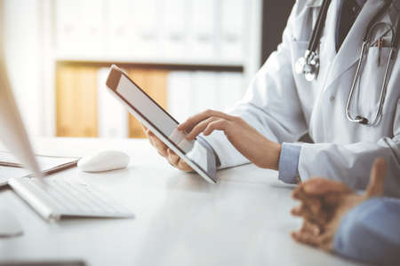 Unknown male doctor and patient woman discussing current health examination while sitting in sunny...