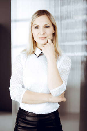 Friendly adult business woman standing straight. Business headshot or portrait in sunny officeの写真素材