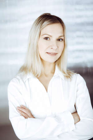 Friendly adult business woman standing straight. Business headshot or portrait in sunny officeの写真素材