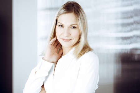 Friendly adult business woman standing straight. Business headshot or portrait in sunny officeの写真素材