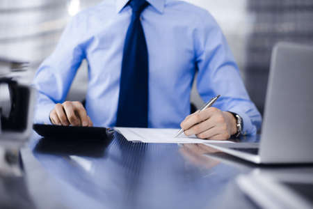 Unknown man accountant in blue shirt use calculator and computer with holding pen on while staying at home during covid pandemic. Taxes and audit conceptの写真素材