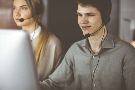 Businessman talking by headset while sitting in sunny office. Telemarketing conceptの写真素材