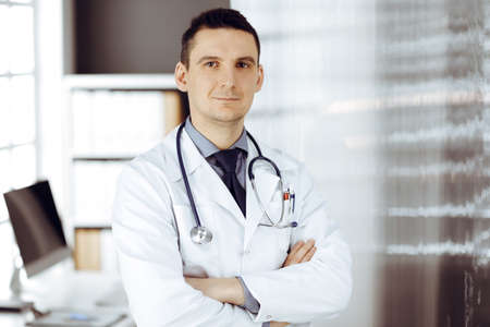 Male doctor standing straight in sunny clinic. Perfect medical service in hospitalの写真素材