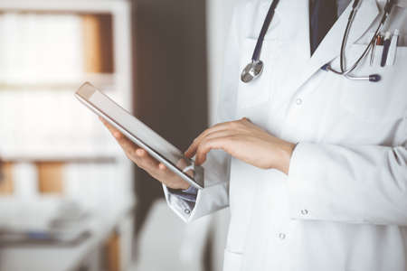 Unknown male doctor using tablet computer in sunny clinic, closeup. Perfect medical service in hospital. Medicine and healthcare conceptの写真素材