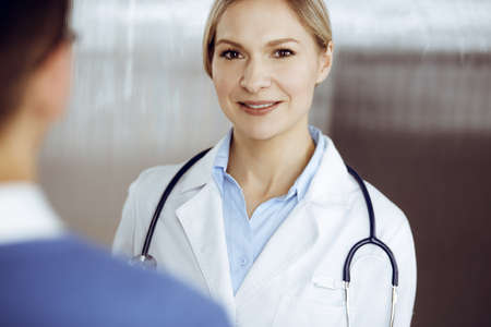 Friendly female doctor and patient man discussing current health examination while sitting in sunny clinic. Perfect medical service in hospitalの写真素材