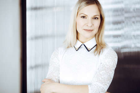 Friendly adult business woman standing straight. Business headshot or portrait in sunny officeの写真素材