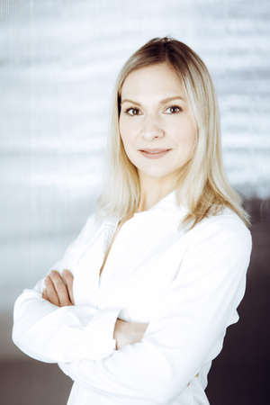 Friendly adult business woman standing straight. Business headshot or portrait in sunny officeの写真素材