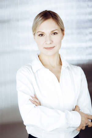 Friendly adult business woman standing straight. Business headshot or portrait in sunny officeの写真素材