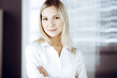Friendly adult business woman standing straight. Business headshot or portrait in sunny officeの写真素材