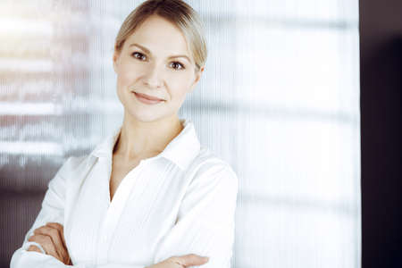 Friendly adult business woman standing straight. Business headshot or portrait in sunny officeの写真素材