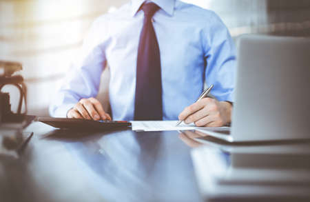 Unknown male accountant use calculator and computer with holding pen on while staying at home during  pandemic. Taxes and auditの写真素材